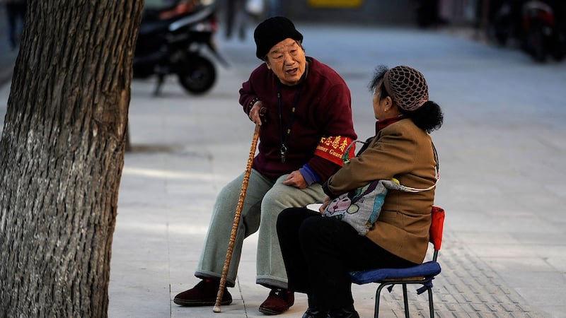 北京,一名戴着红袖章的老年志愿者(左)在路边与一名中国妇女交谈。 (法新社)