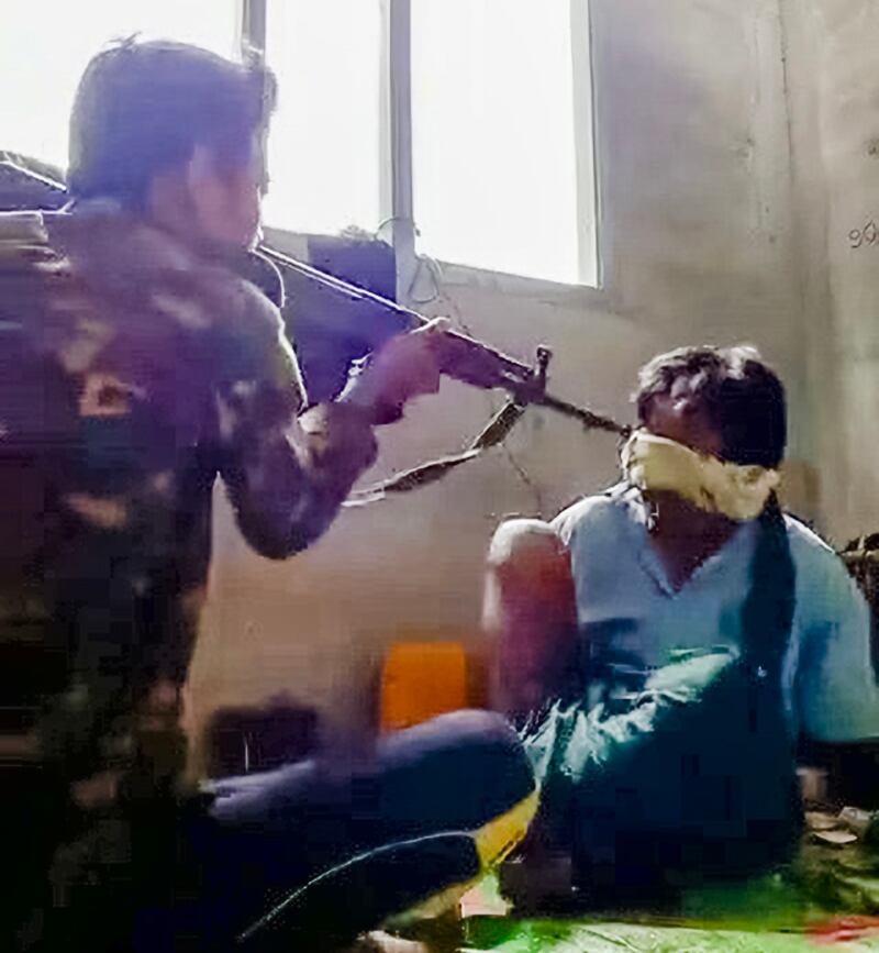 မျက်နှာတွင်အဝတ်စည်းကာ လက်နောက်ပြန်ကြိုးတုပ်ပြီး ဖမ်းဆီးခံထားရသည့် အရပ်သား၏ဦးခေါင်းကို စစ်ကောင်စီတပ်မ-၆၆ လက်မောင်းတံဆိပ်ပါ ယူနီဖောင်းဝတ်ဆင်ထားသည့် စစ်သားက ရိုင်ဖယ်သေနတ်ဖြင့် ချိန်ထားစဉ်။ (RFA screenshot from video)