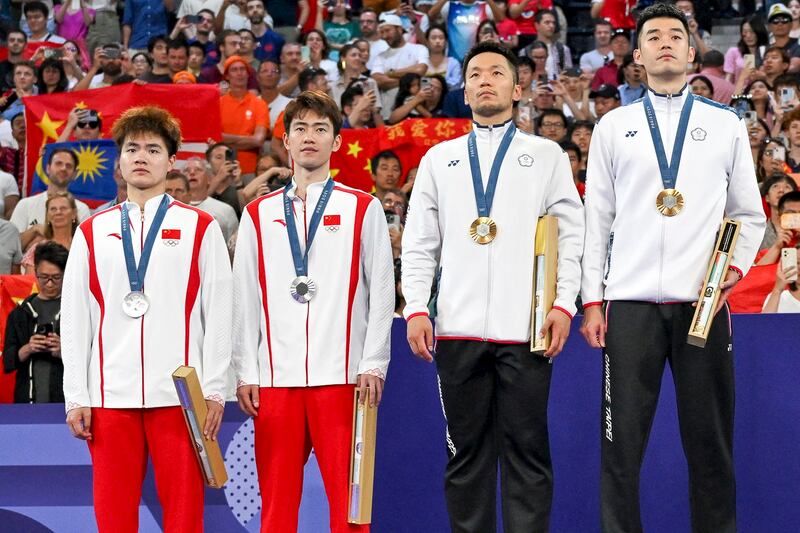 Taiwan's gold medalists (R) Lee Yang and Wang Chi-lin and China's silver medalists Liang Weikeng and Wang Chang stand up for the anthem of Chinese Taipei on the podium at the men's doubles badminton medal ceremony during the Paris 2024 Olympic Games at Porte de la Chapelle Arena in Paris, Aug. 4, 2024. (Arun Sankar/AFP)