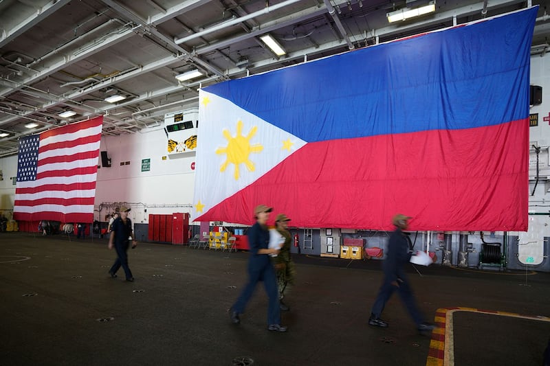 2022年10月14日,美国军人在罗纳德·里根号航空母舰(CVN 76)内悬挂的菲律宾和美国国旗旁边行走。(美联社)