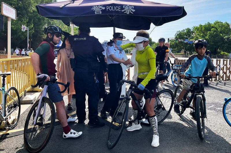 2023年6月4日,一名骑车的外国人(左一)在北京东长安街的安检点等待身份检查。(美联社)