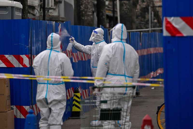 2022 年 3 月 23 日,北京一名身穿防护服的保安在一个封闭社区的门口喷洒消毒剂。 (美联社)